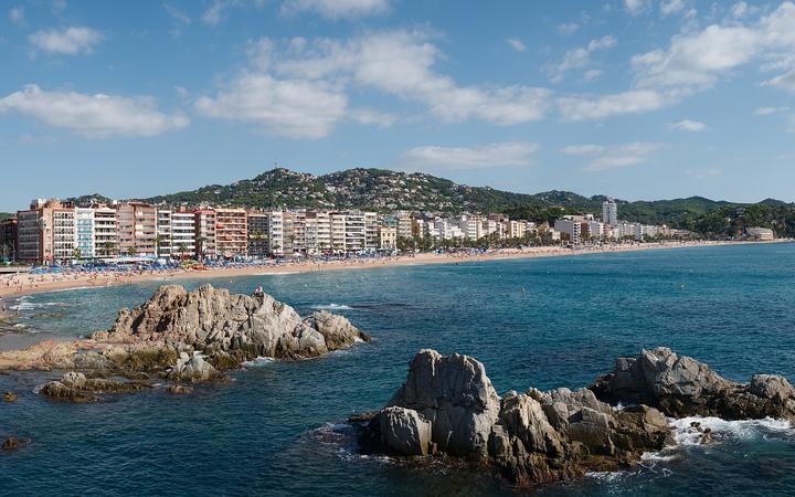 Het strand van Lloret de Mar met de boulevard en groene heuvels op de achtergrond